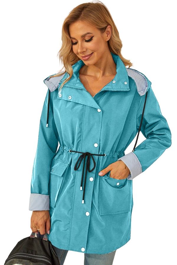 woman wearing blue water resistant windbreaker with hood and striped details holding black bag