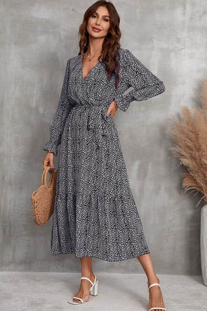 Woman wearing Bloom Wrap Midi Dress with floral print, long sleeves, and A-line silhouette, holding a woven handbag.
