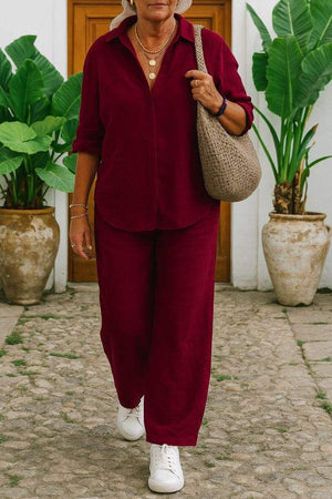 Woman wearing maroon relaxed shirt and trousers two-piece set with white sneakers and beige woven bag outdoors