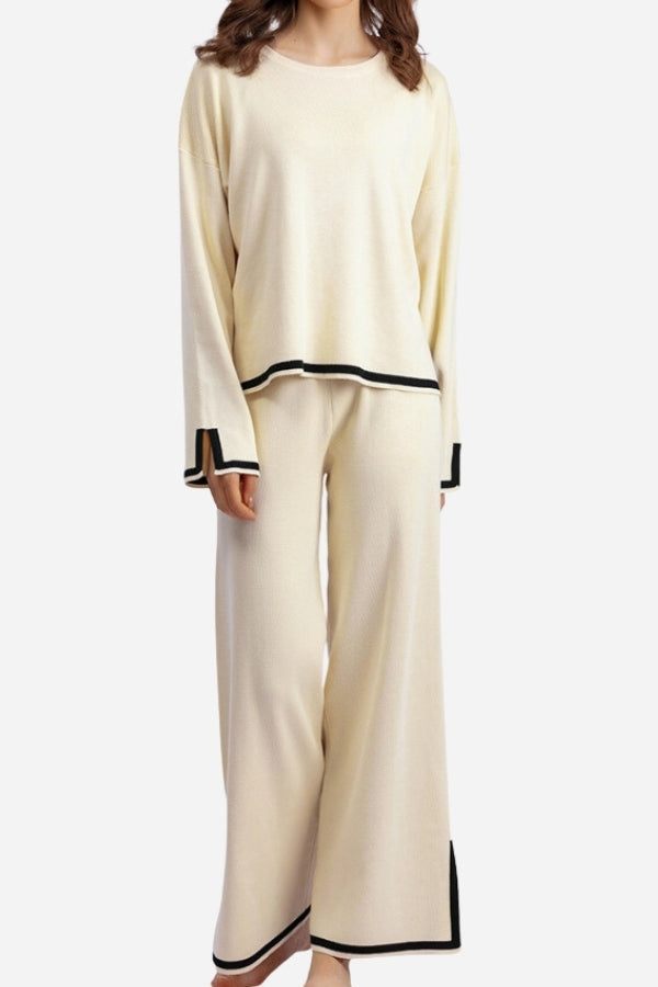 Woman wearing cream long sleeved relaxed fit lounge two-piece set with black trim on cuffs, hem, and pant edges