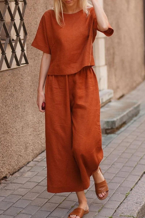 Woman wearing rust-colored loose fit co-ord set with short sleeves and wide-leg pants walking on a city sidewalk