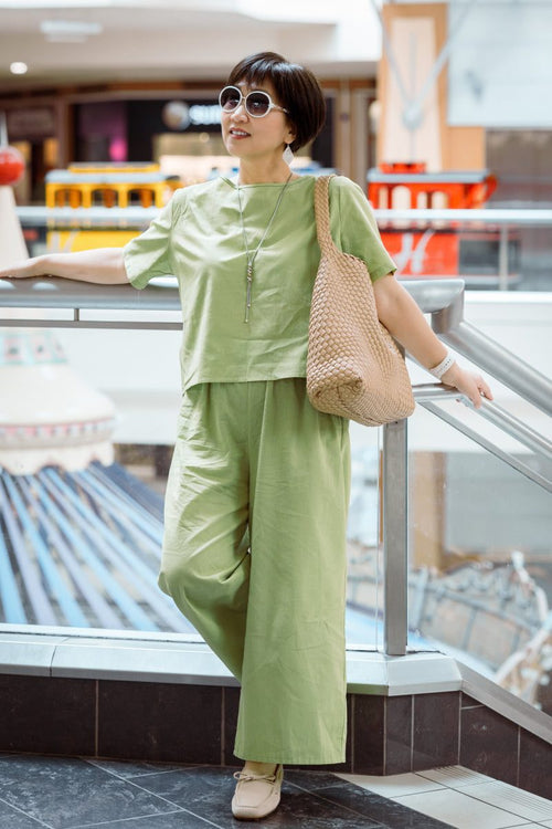 Woman wearing green loose fit co-ord set with wide-leg trousers and short-sleeve top, styled with sunglasses and a woven handbag.