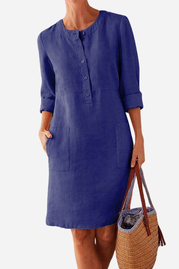 Blue cotton dress with button front, 3/4 rolled sleeves, and pockets, styled with a woven handbag.