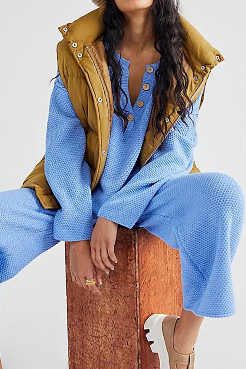 woman wearing multi-weather comfort two-piece oversized set with blue knit top and pants and brown vest sitting on wooden block