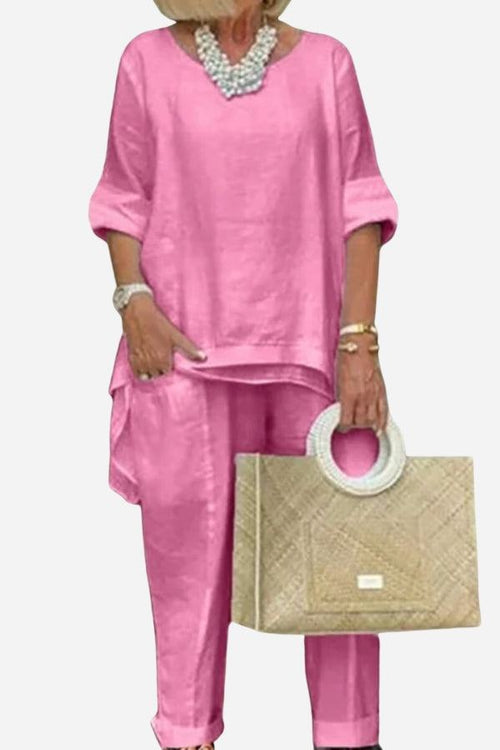 Pink asymmetrical two-piece trouser set with rolled sleeves and tapered pants on model holding woven handbag