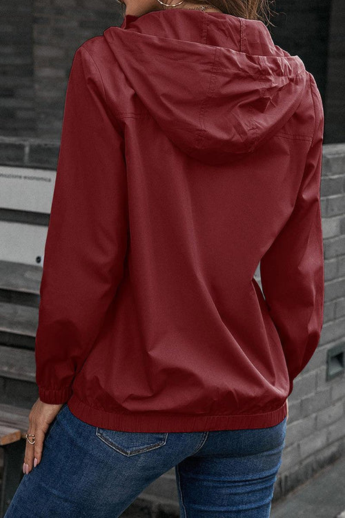 Red outdoor hooded raincoat and windbreaker with elastic cuffs and hem, worn with blue jeans, shown from the back