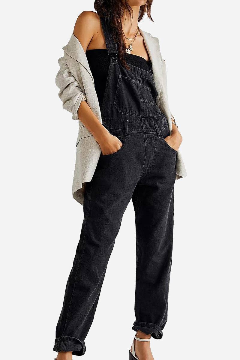 Woman wearing black denim-look tapered-leg adjustable bib overalls with a gray blazer and black top.