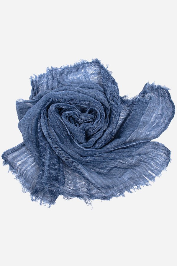 Blue lightweight linen scarf with frayed edges, folded and curled on a white background