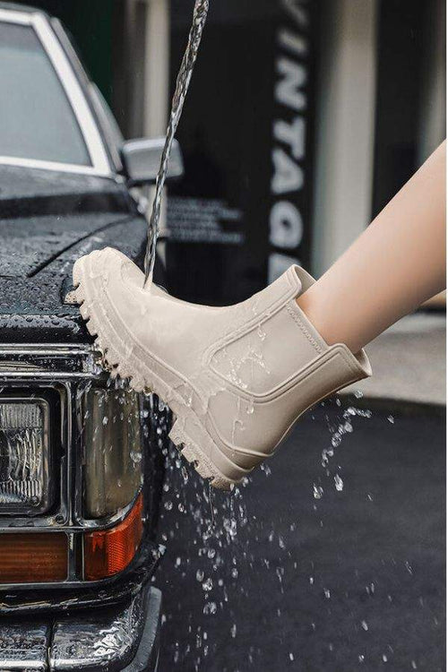 Light beige non-slip rain boots with SuperGrip sole being splashed with water, demonstrating waterproof feature.