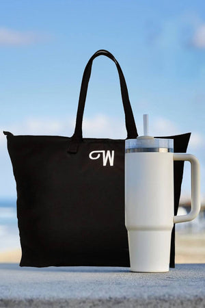 White indestructible travel cup with handle and straw next to black tote bag against blue sky background