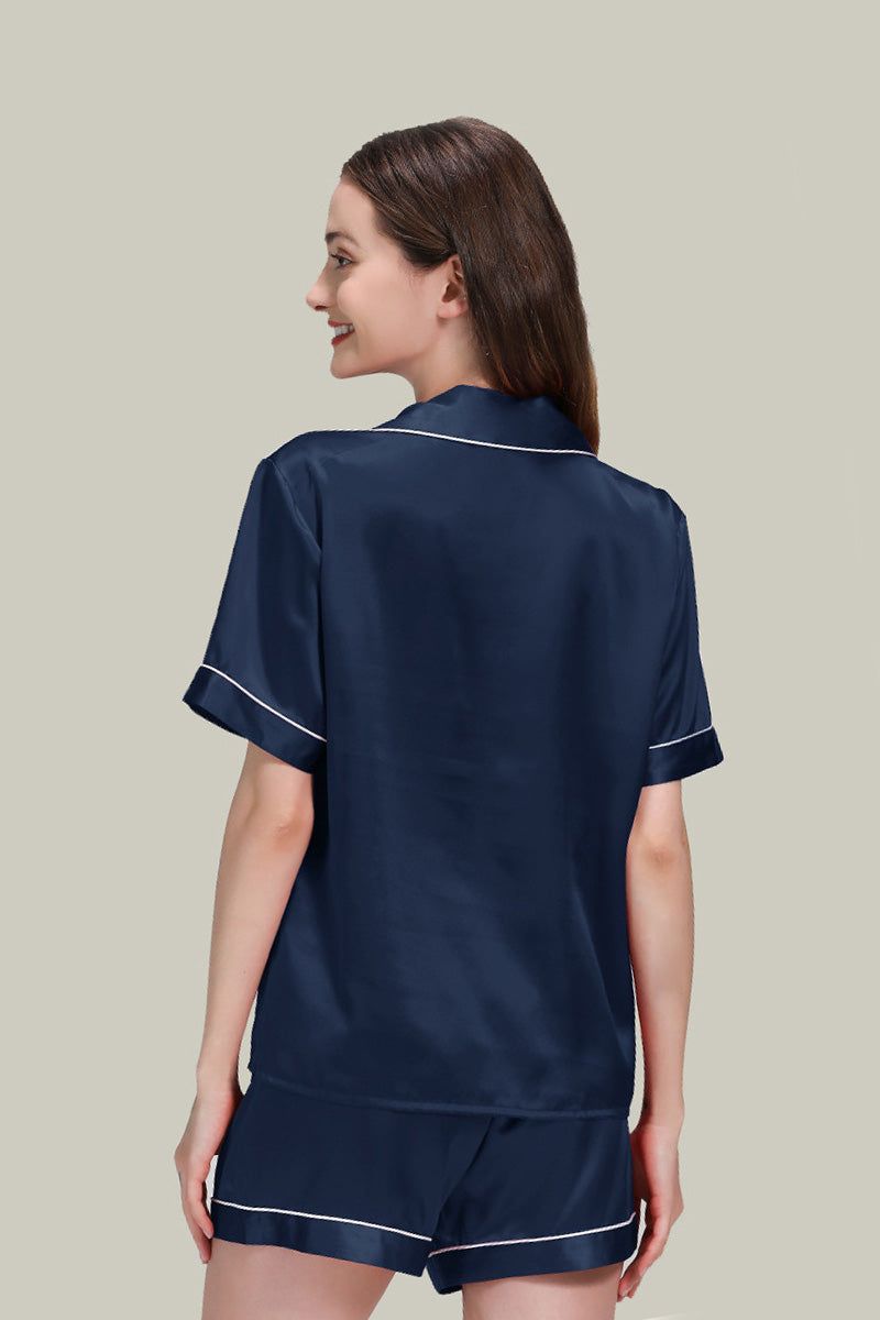 Back view of woman wearing navy blue Mulberry silk buttoned short set nightwear with white piping trim.