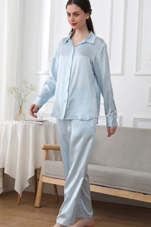 Woman wearing light blue Mulberry silk sleepwear set with long-sleeve button-up top and matching pants in a cozy room.