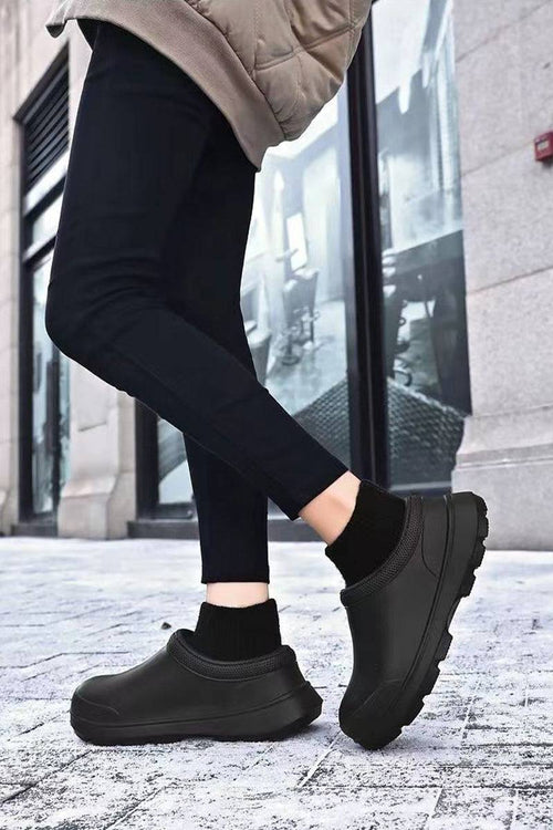 Black fleece-lined comfort clogs with durable waterproof rubber soles worn outdoors on city pavement