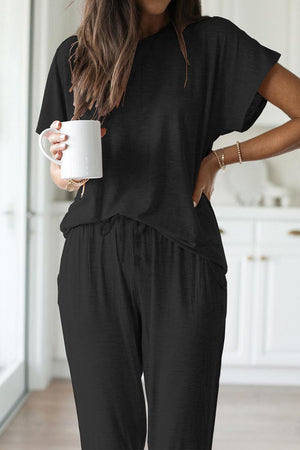 Woman wearing black ultra-soft two-piece loungewear set with batwing sleeves and jogger pants holding a white mug indoors