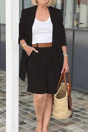 Stylish blazer and shorts two-piece set in black, worn with white top and brown belt, accessorized with woven tote bag.