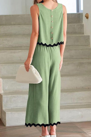 Back view of woman wearing green scalloped trim sleeveless top and wide leg pants set with button details and black scalloped edges.