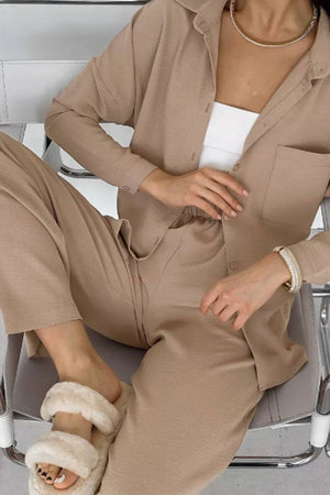 Beige relaxed fit wide-leg two-piece set with a button-up shirt and elastic waist pants, styled casual with fluffy slippers and gold jewelry.