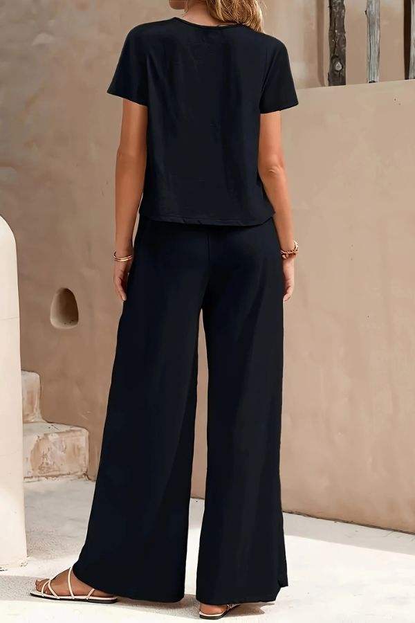 Woman wearing Riviera Relaxed Two Piece Set in black, featuring a loose short-sleeve top and wide-leg pants from the back.