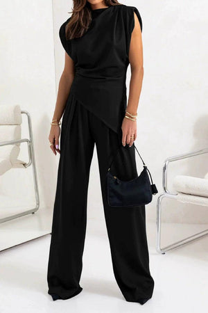 Woman wearing black Manhattan Lines Draped two-piece set with asymmetrical draped sleeveless top and wide-leg palazzo pants.