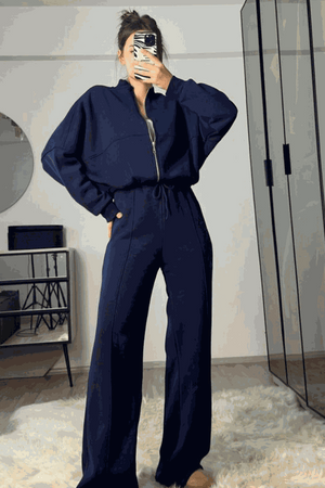 Woman wearing navy blue The Voyager Zip Set with zip-front sweatshirt and wide-leg joggers in a modern room with mirror and shelves