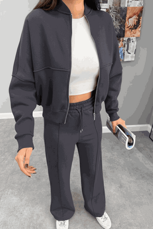 Woman wearing The Voyager Zip Set in dark gray with zip-front sweatshirt and wide-leg joggers, styled casually with a white crop top and sneakers.