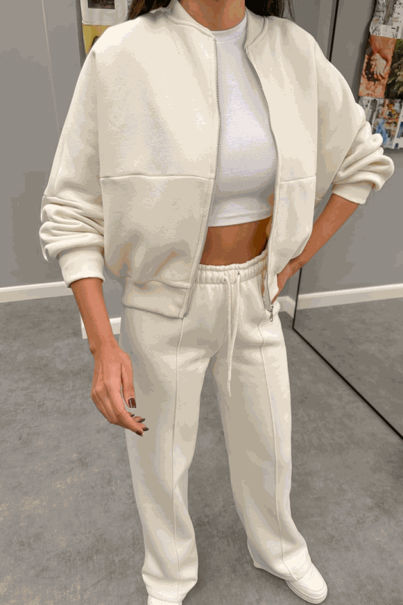 Woman wearing The Voyager Zip Set cream zip-front sweatshirt and wide-leg joggers with pockets, styled with a white crop top and sneakers.