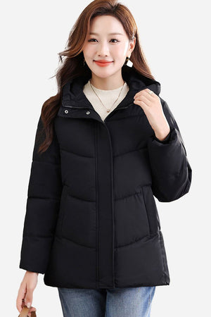 Woman wearing black mid-length Everyday Warmth Coat with hood and relaxed fit standing against white background