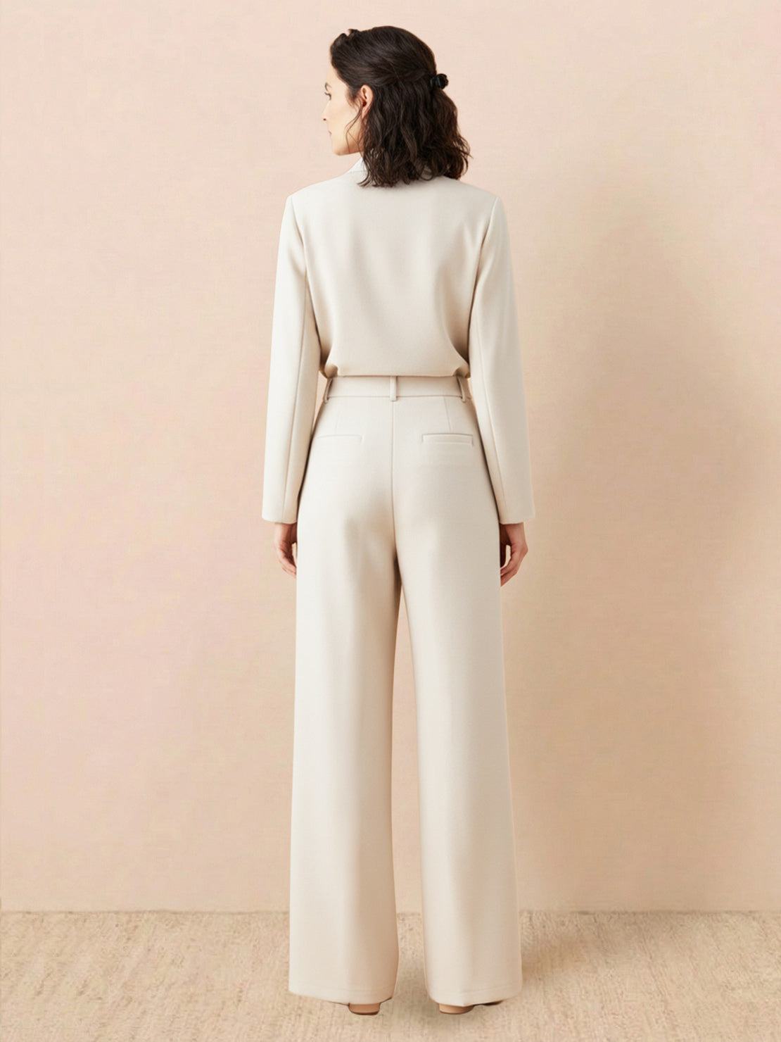 Woman wearing beige wide-leg thermal wool blend trousers with elastic back waist, standing against plain background, rear view.