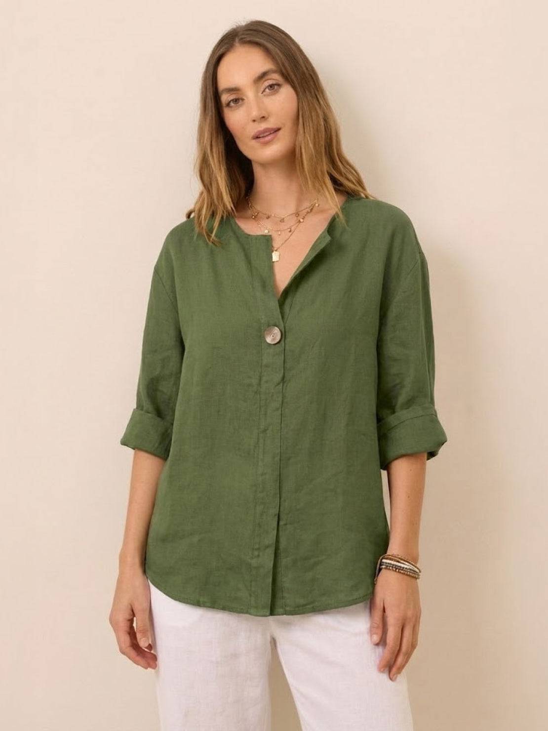 Woman wearing green pure linen age-defying button detail shirt with rolled-up sleeves and white pants