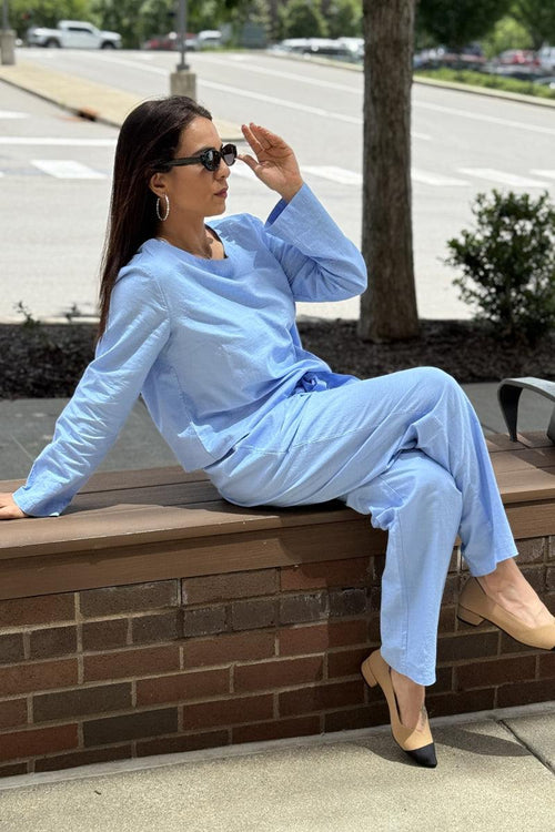 Woman wearing a light blue cotton-linen monochrome capsule outfit with longline top and wide-leg pants sitting outdoors
