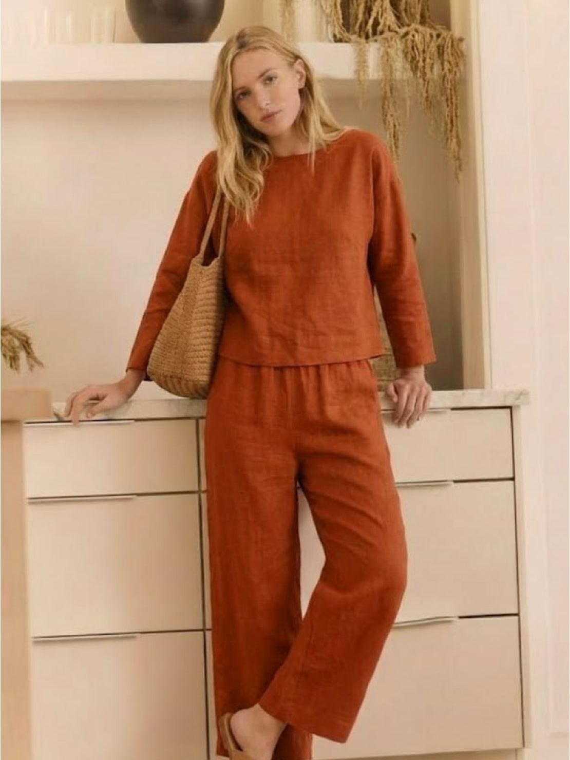Woman wearing loose solid color two-piece set with long sleeves and wide-leg pants in rust orange color indoors