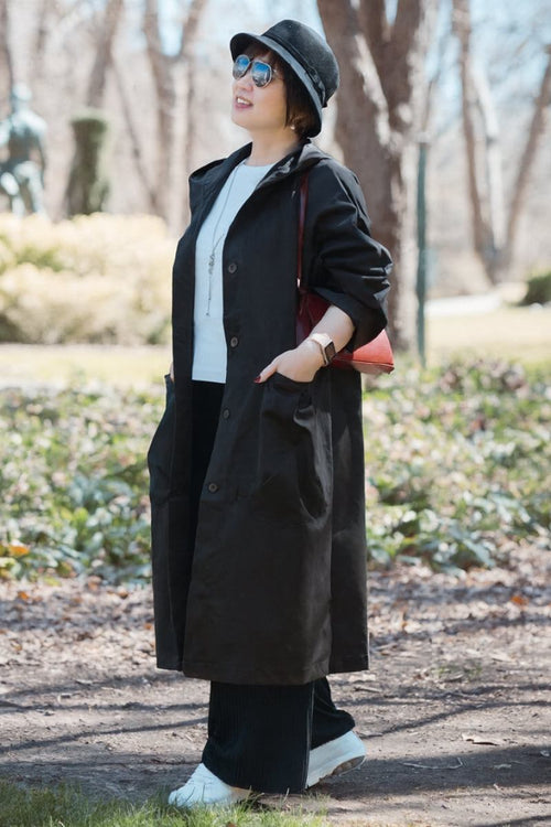 Woman wearing oversized black water resistant windbreaker jacket with attached hood and snap-button closure outdoors