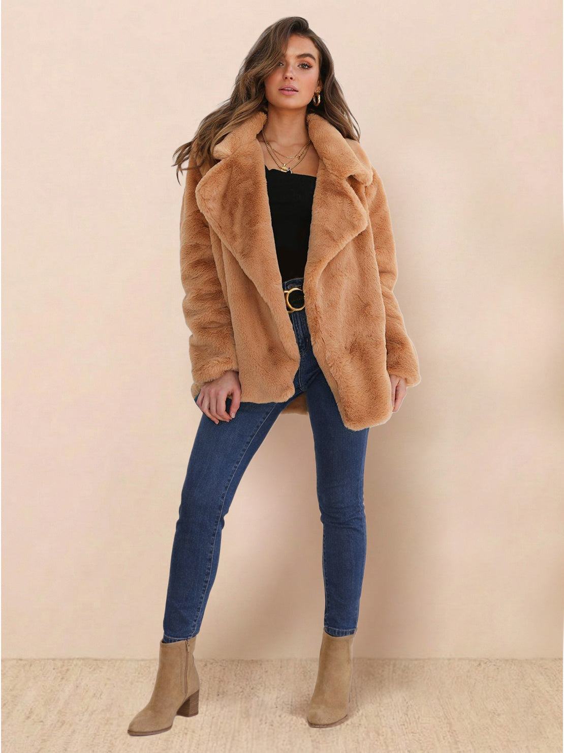 Woman wearing camel open front oversized faux fur jacket with draped collar, paired with blue jeans and beige ankle boots