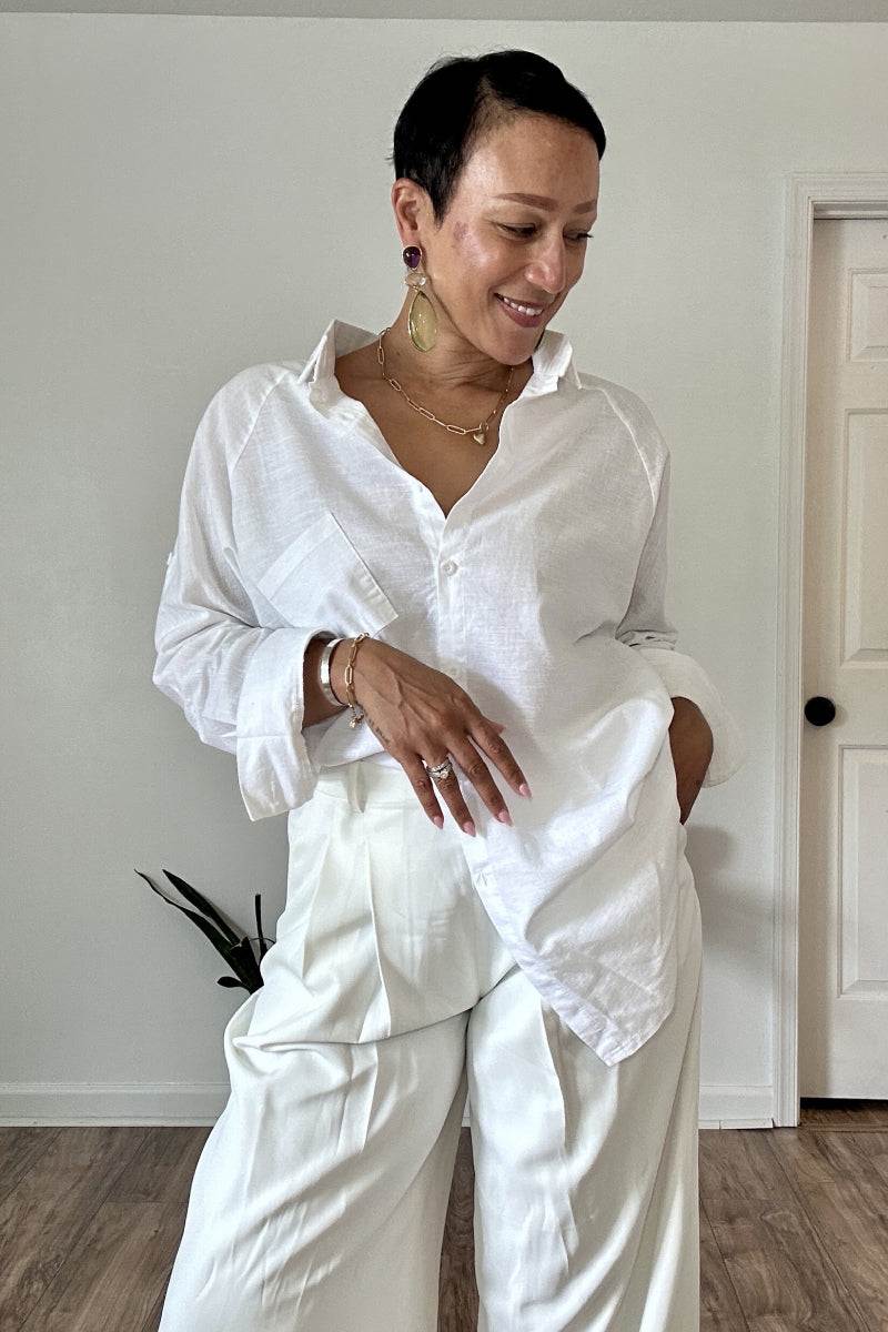 Woman wearing a white oversized linen shirt with relaxed fit and flowing hem paired with white pants indoors
