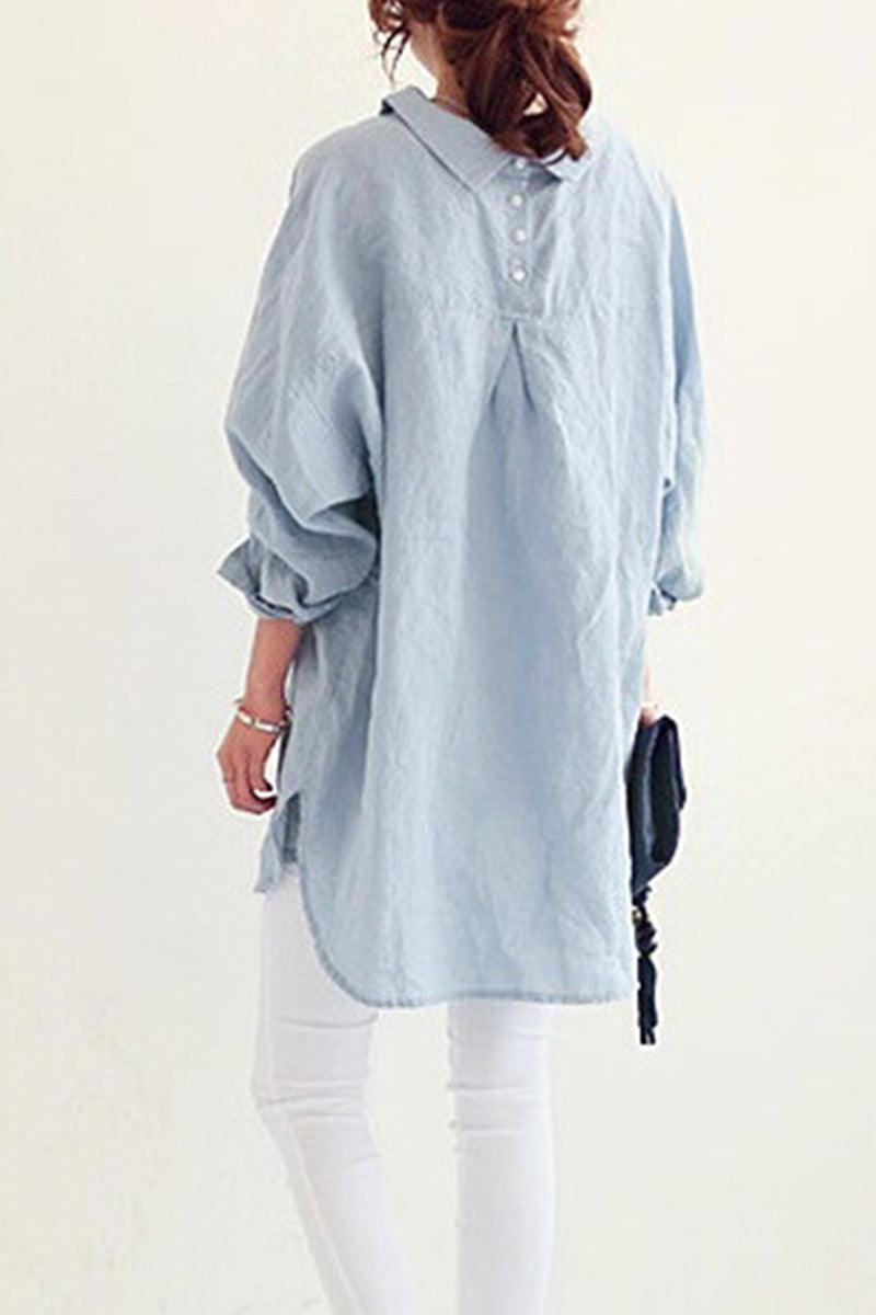 Back view of woman wearing light blue oversized linen shirt with rolled sleeves and white pants