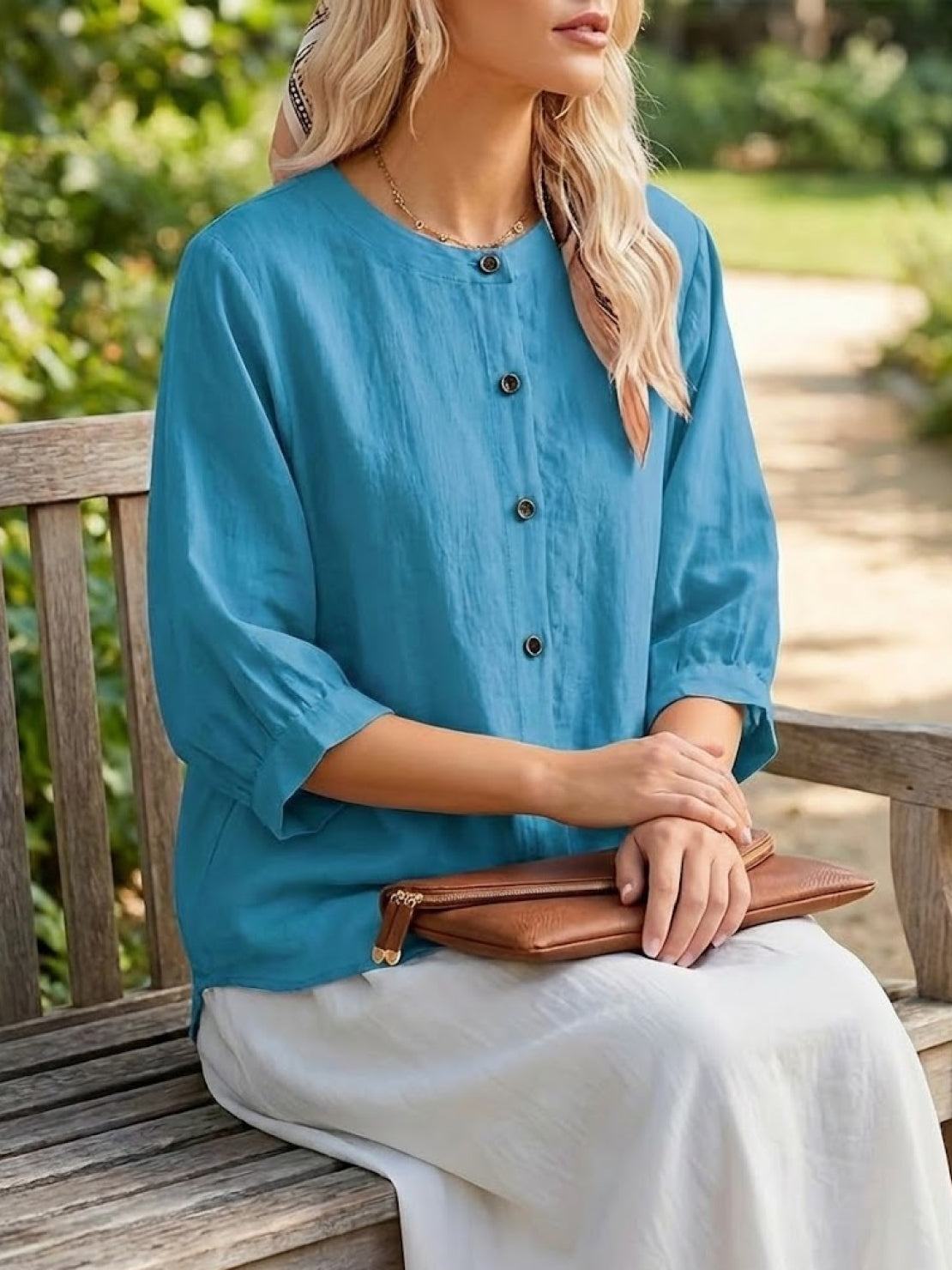 Relaxed loose breathable linen blouse in vibrant blue with button-down front and three-quarter sleeves, styled casually outdoors