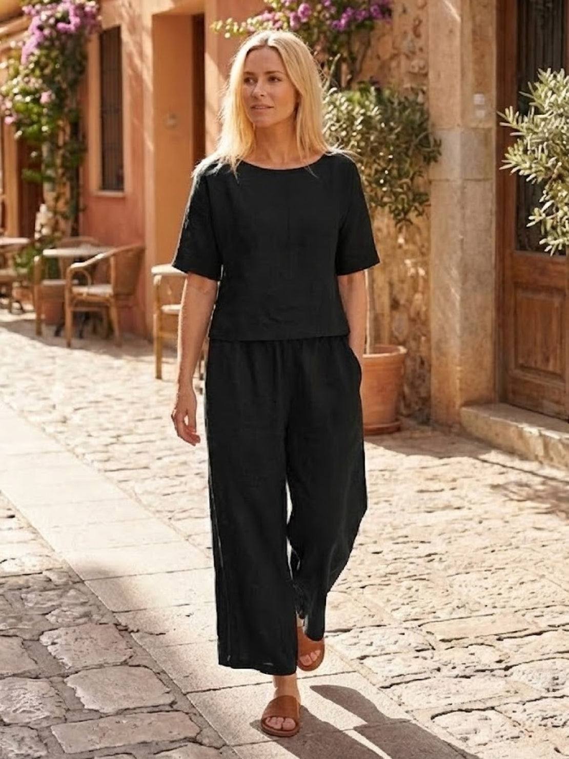 woman wearing black loose fit co-ord set with short sleeves and wide-leg trousers walking outdoors on sunny stone pathway