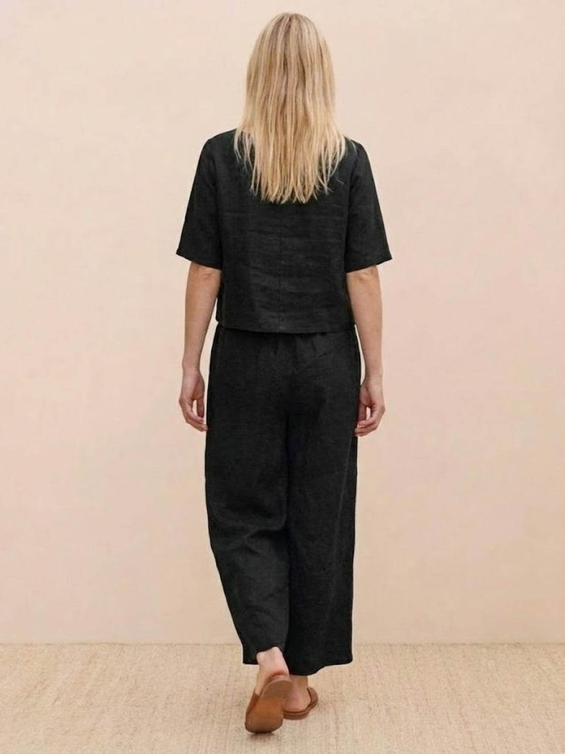 Back view of a woman wearing a black loose fit co-ord set with a soft-tailored top and wide-leg bottoms.