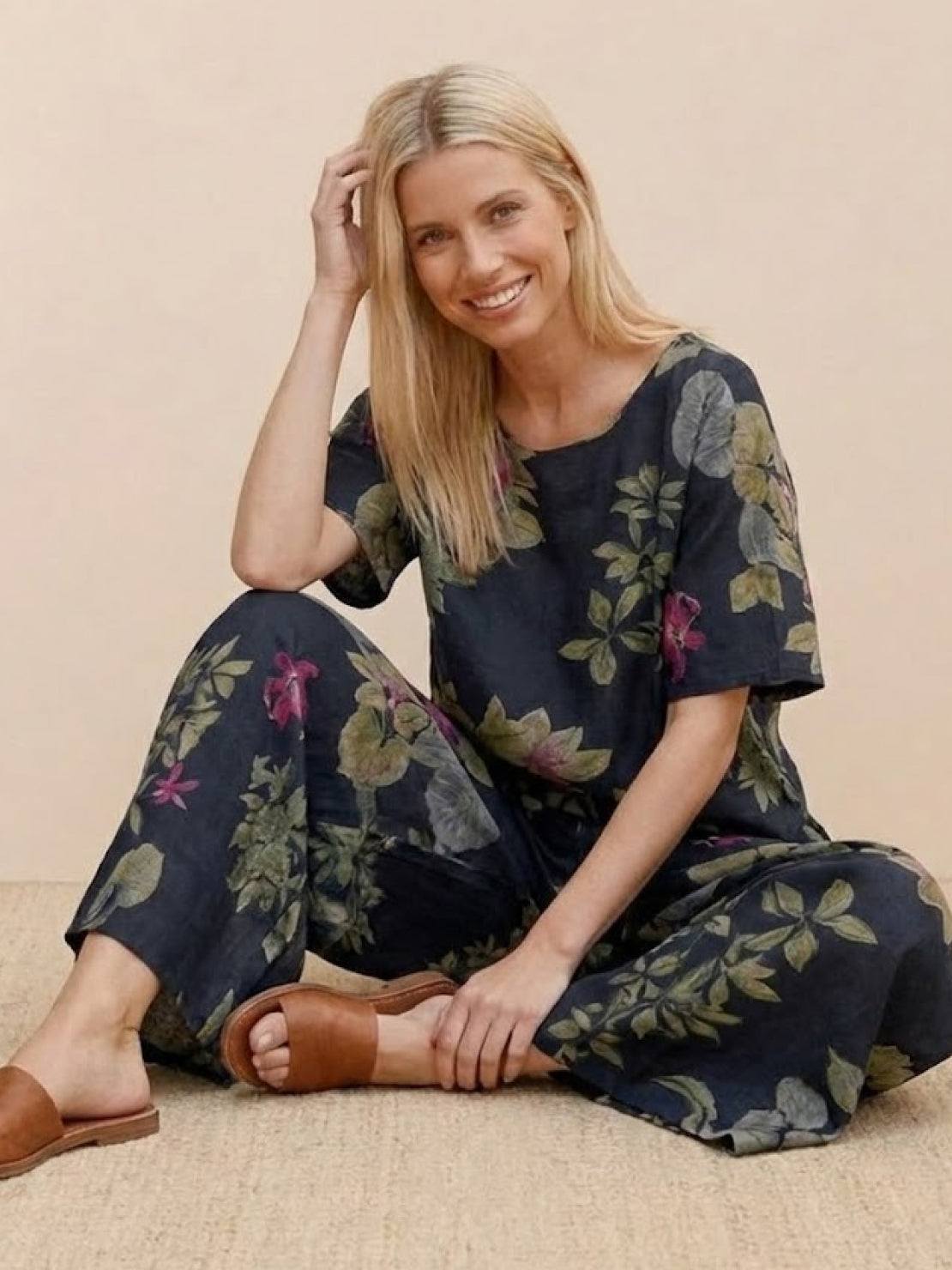 Woman wearing a loose fit co-ord set with wide-leg floral print trousers and a soft-tailored short sleeve top, styled casually with sandals.