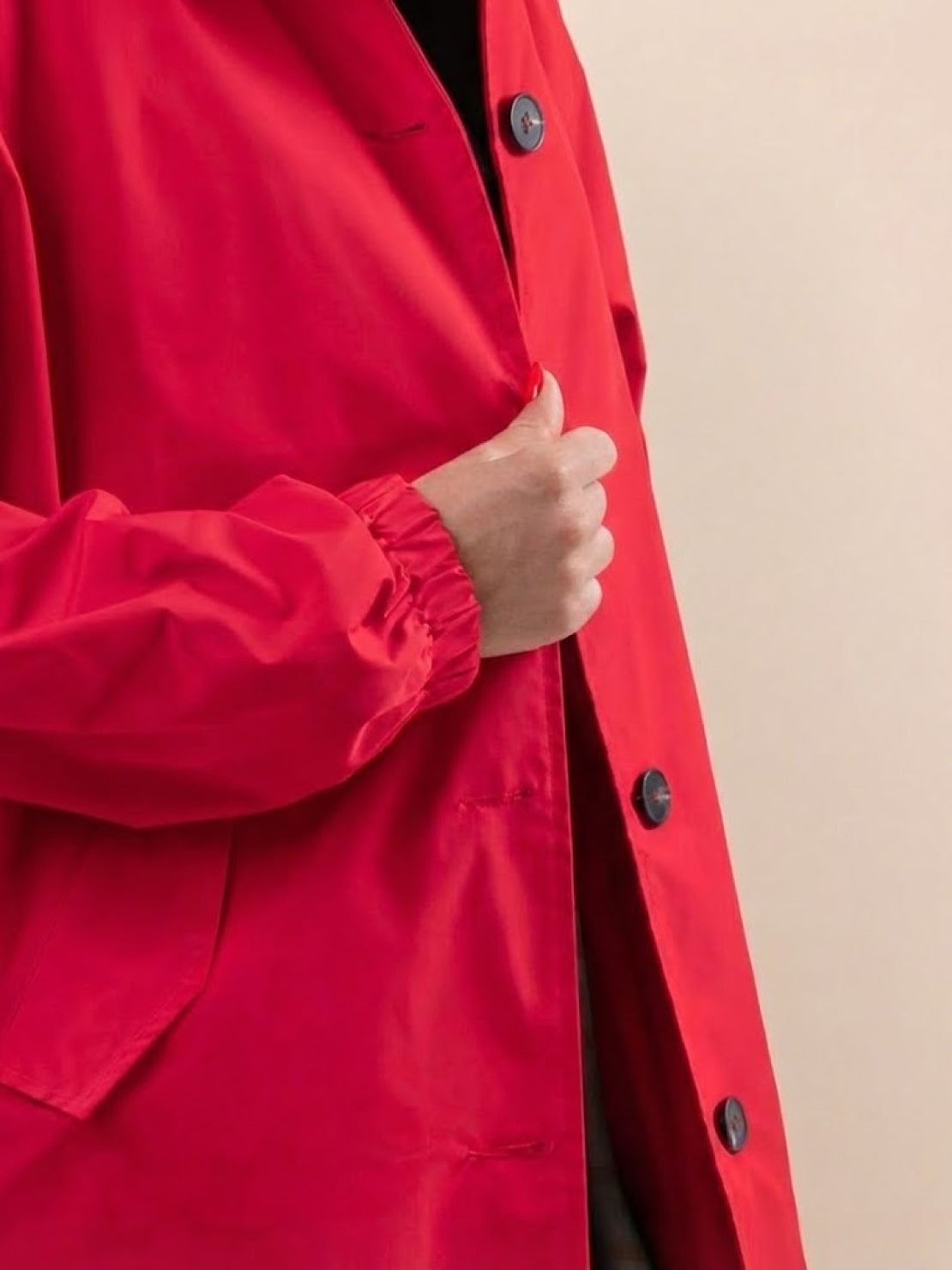 Close-up of a vibrant red Rain Couture Windbreaker with button closure and elastic cuff.