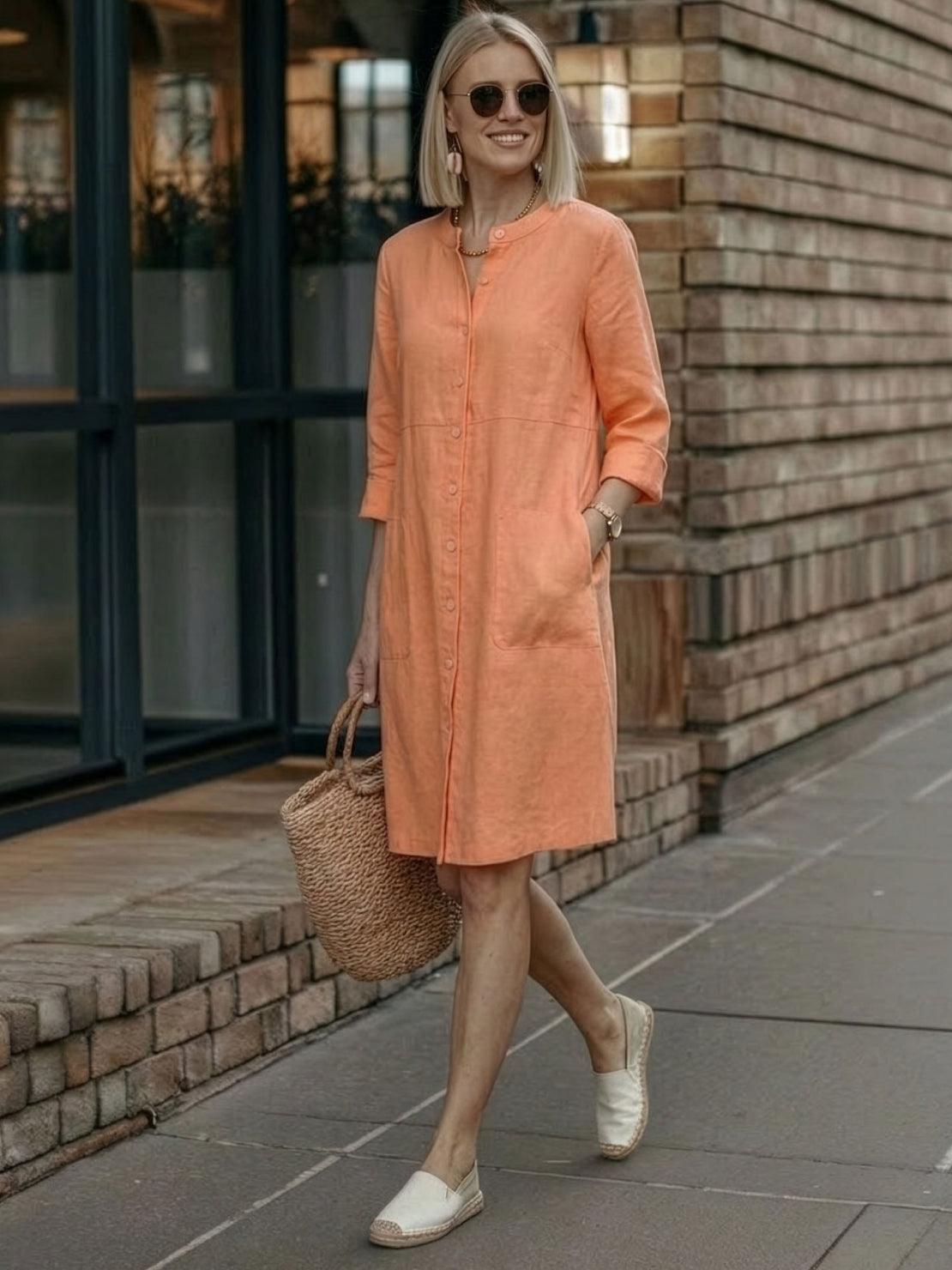 Woman wearing a lightweight orange cotton dress with buttons and 3/4 sleeves carrying a woven bag outdoors