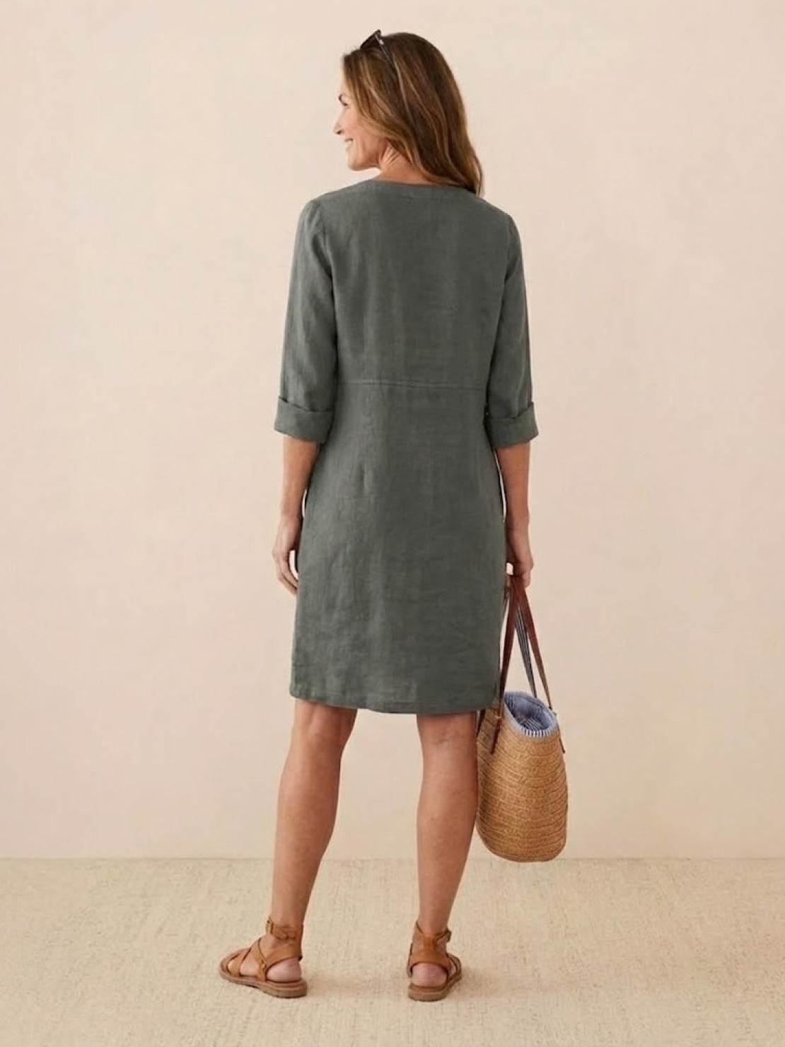 Back view of woman wearing knee-length green cotton dress with rolled ¾ sleeves and carrying straw tote bag