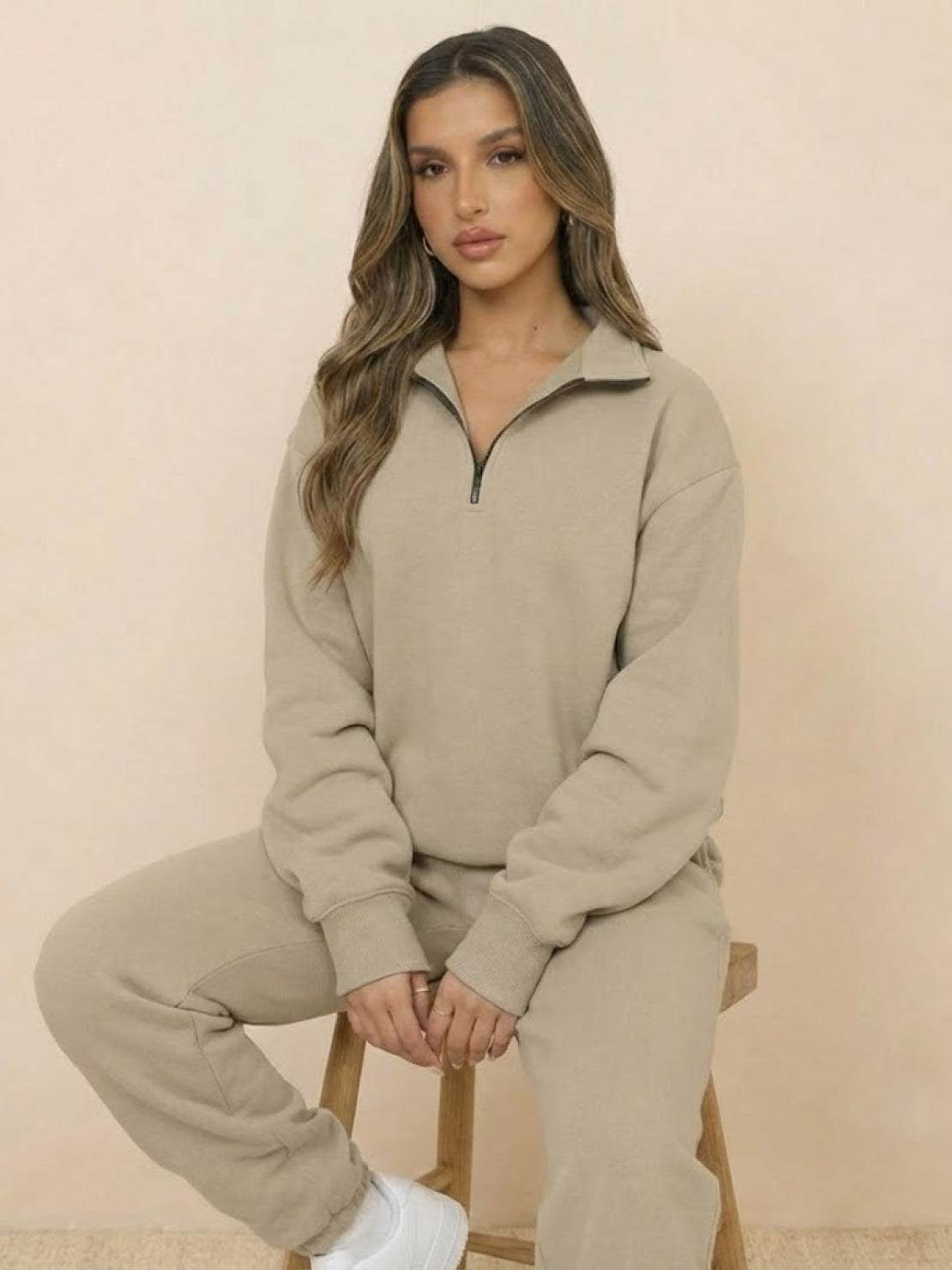 Woman wearing beige ultra-soft and comfy co-ord tracksuit set with zip-up top sitting on stool.