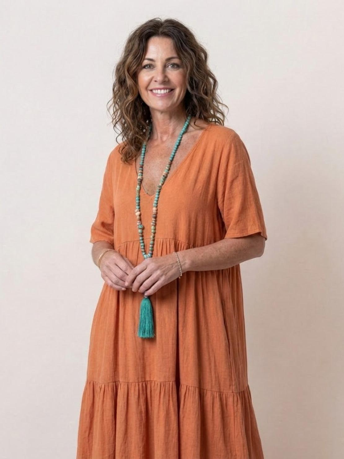 Woman wearing V-neck two-tiered maxi swing dress in flowing cotton fabric with irregular hemline and loose sleeves