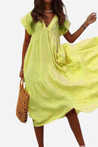 Woman wearing a light green V neck tiered cotton midi dress with short sleeves and frill hem holding a woven handbag