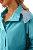 Close-up of woman wearing turquoise water resistant windbreaker with hood and striped lining
