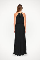 Back view of a woman wearing a black sleeveless belted maxi pleated dress with a keyhole neckline.