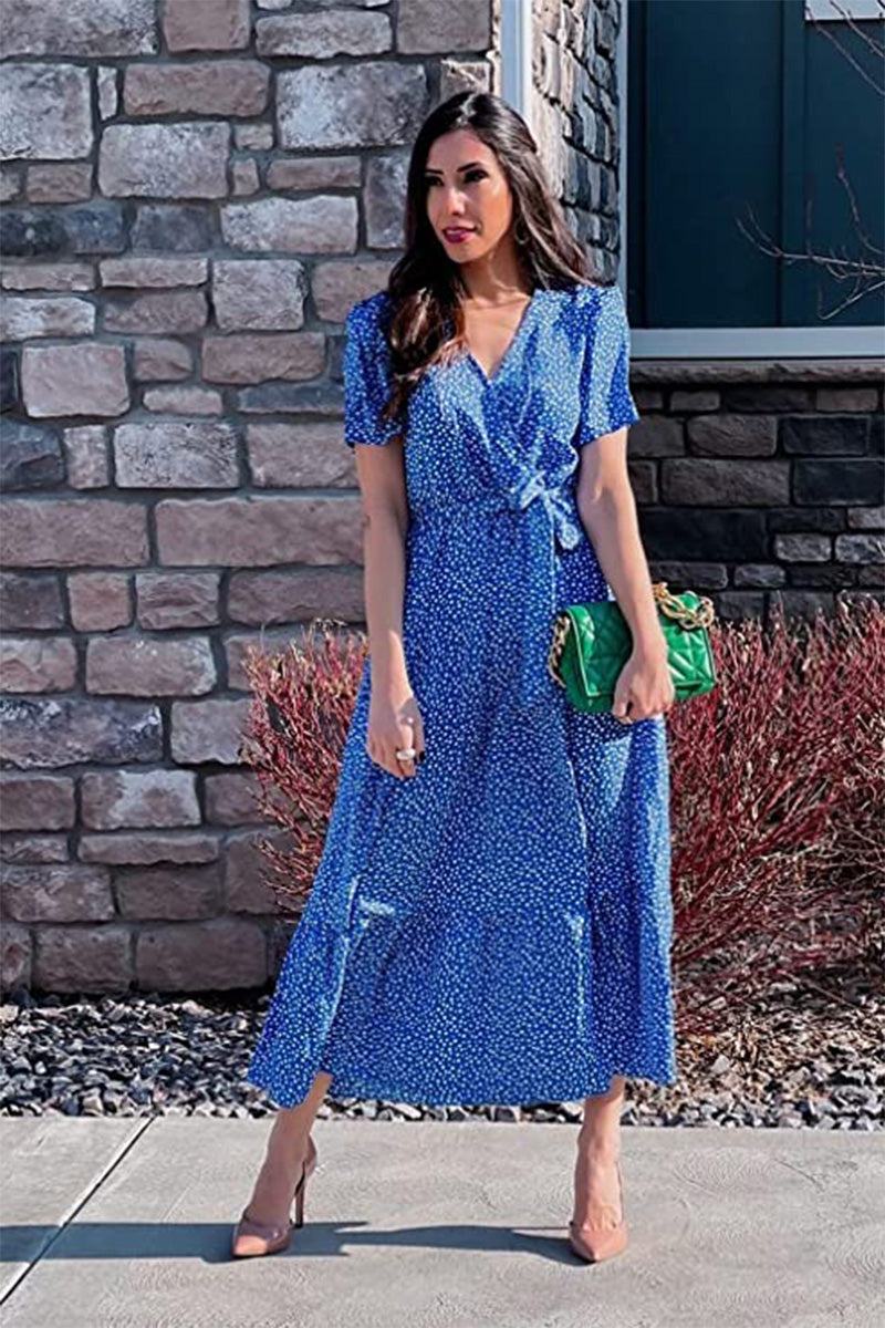 Woman wearing a blue charming floral boho maxi dress with short sleeves and a wrap V-neck standing outdoors near a stone wall.