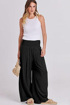 Woman wearing oversized shirt and palazzo pants two-piece linen set with black wide-leg pants and white sleeveless top