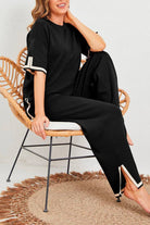 Woman wearing black short sleeved relaxed fit two-piece lounge set sitting on a wicker chair